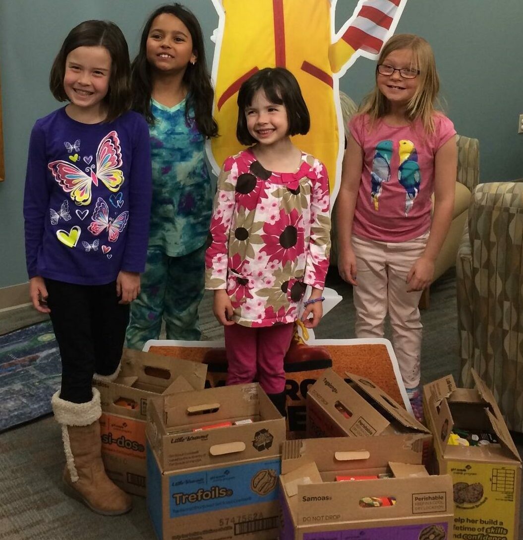 Four Girl Scouts posing with cookies that they donated in front of a Ronald McDonald Cut-Out
