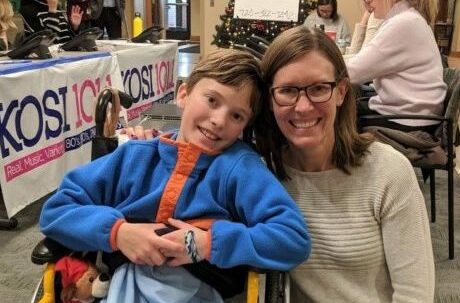 Smiling woman kneeling beside smiling boy in a wheel chair at the radiothon