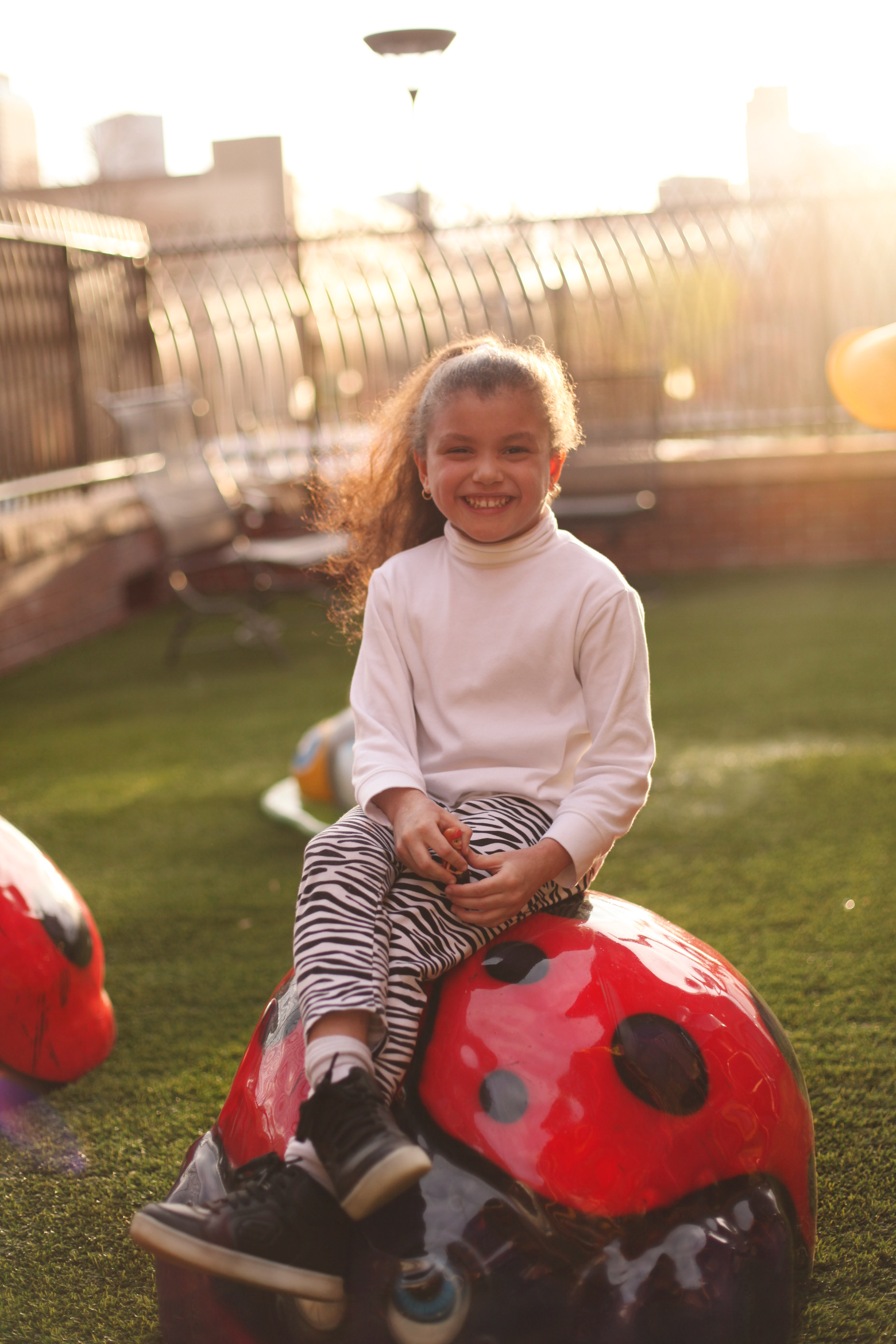 Young smiling girl sitting on a ladybug on the playground