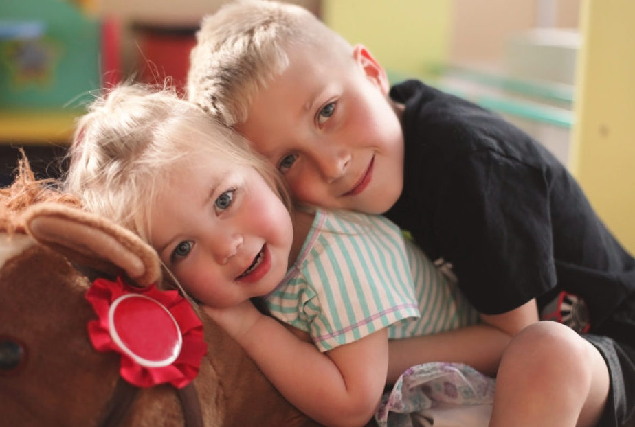Brother and sister hugging while sitting on a stuffed horse