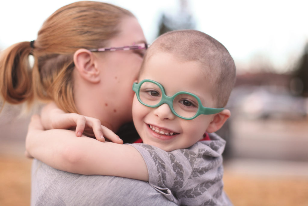 Small boy in glasses embracing his Mom around her neck