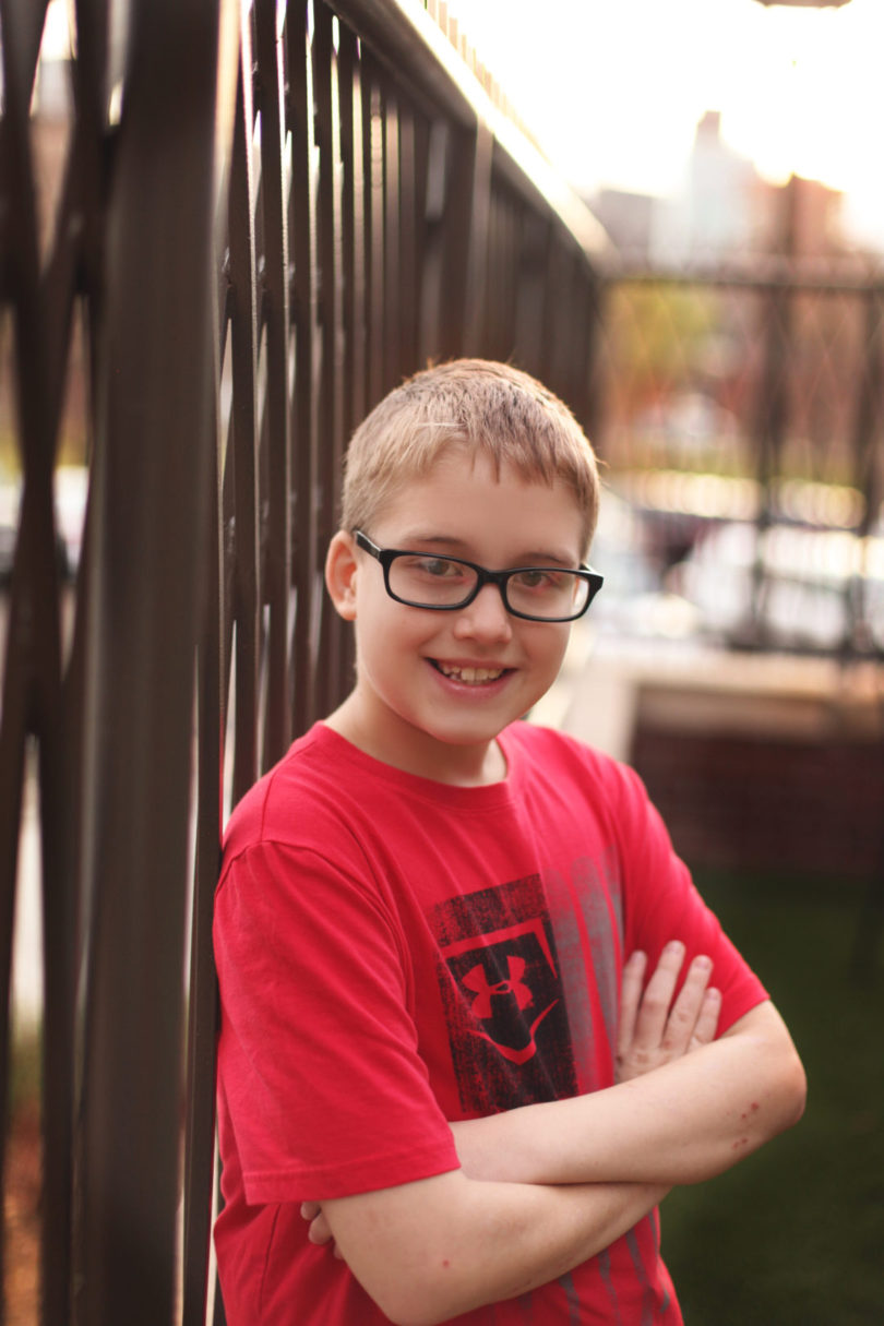Smiling young man in glasses leaning against a fence